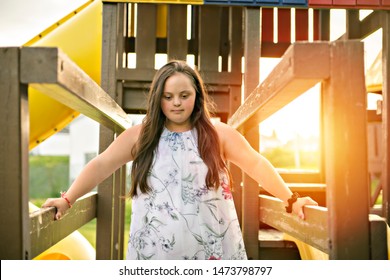 A portrait of trisomie 21 adult girl outside at sunset having fun on a park