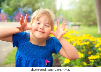 A portrait of trisomie 21 child girl outside having fun on a park giving some grim
