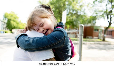 A portrait of trisomie 21 child girl outside hugging his mother on a school playground