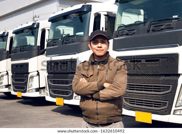 Portrait of truck driver standing cross\
one’s arm looking with smile, Trucks parked lined up\
