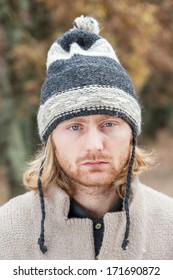 Portrait, Twenty Four Year Old Man With Blue Eyes And Long Blonde Hair, Wearing A Woolen Hat In A Day Of Winter In A Forest. 