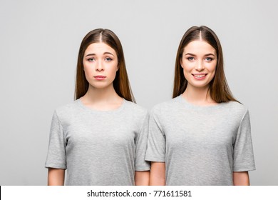 portrait of twin sisters in grey tshirts showing emotions isolated on grey