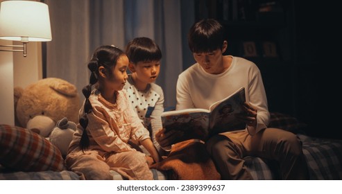 Portrait of Two Active Children Engaged in a Conversation with their Father While He Reads to them Before Bed. Cute Korean Kids not Ready to Go to Sleep, Reading a Story With their Male Parent - Powered by Shutterstock