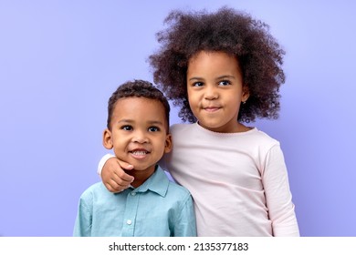 portrait of two adorable siblings brother and sister hugging each other, isolated on purple studio background. portrait of black birl and boy in casual wear posing looking at camera