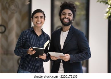 Portrait of two ambitious young 30s Indian male female colleagues pose in workspace smile look at camera, hold personal organizer and digital tablet. Professional occupation people, team-work, career