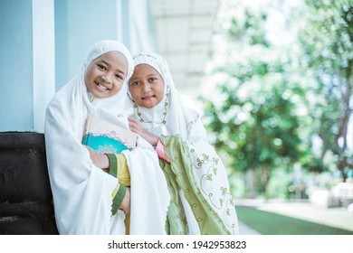 Portrait two Asian Muslim girls wearing mukena holding al quran book after salat together