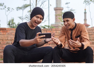 Portrait Of Two Asian Muslim Man Sitting In City Park And Talking To Each Other And Watching News On Mobile Phone Together