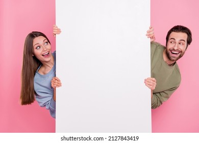 Portrait of two astonished positive persons peek look empty space sale promotion isolated on pink color background