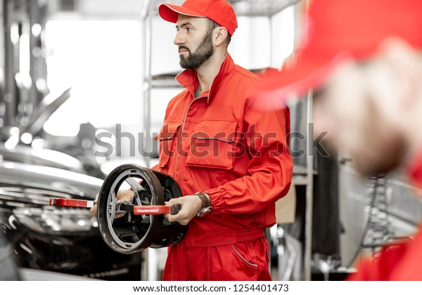 Portrait of a two auto\
mechanics in red uniform standing with disks for wheel alignment at\
the car service