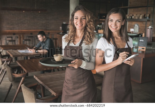 portrait of two beautiful female waitress smiling\
to camera