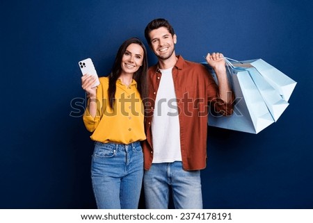Portrait of two beautiful partners hold store bags use smart phone online order isolated on blue color background