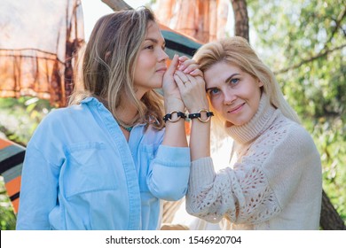 Portrait Of Two Beautiful Women Brunette And Blond Holding Their Hands With Same Bracelets Next To The Tree In Late Summer. Concept Of Harmony, Nature, Naturalness, Fashion, Style, Friendship