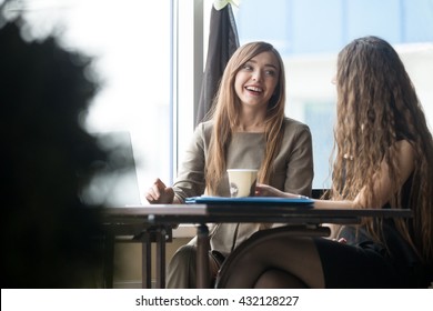 Portrait of two beautiful young girlfriends sitting in modern coffee shop interior and talking with happy smiles. Successful attractive women friends chatting in cafe during coffee break - Powered by Shutterstock