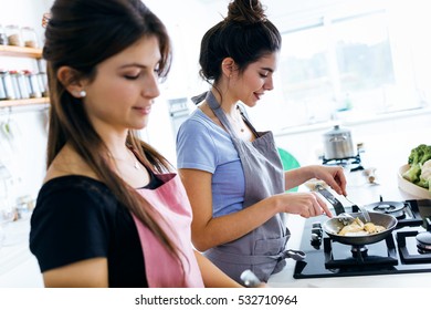 Portrait Of Two Beautiful Young Women Cooking Chicken Breast In The Pan.