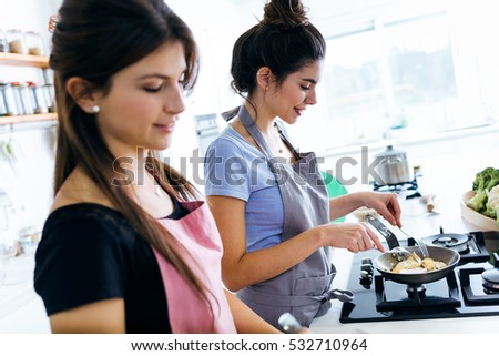Portrait of two beautiful young women cooking chicken breast in the pan.
