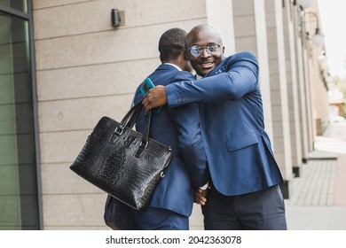 Portrait Of Two Black African American Businessmen In Suits Shaking Hands And Hugging Tightly Outdoors. The Joy Of Meeting Good Friends