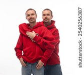 Portrait of two brothers posing in matching casual style outfits against white studio background. Twins hugs and looking at camera calmly. Concept of relationships, brotherhood, family, fun and joy.