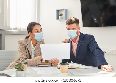 Portrait Of Two Business People Man And Woman Wearing Masks Looking At Documents During Meeting At Post Pandemic Office