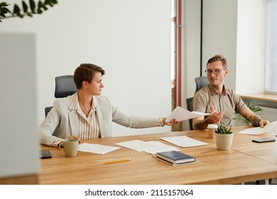 Portrait Of Two Business People Reviewing Documents While Sitting At Desk In Modern Office