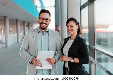 Portrait Of Two Business People Standing In Office Lobby.