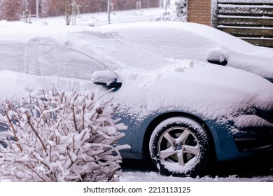 A Portrait Of Two Cars Covered In White Snow Parked In A Driveway. The Driver Will Have To Clear All Windows From Snow Or Wait For The Snow To Melt In Order To Start Driving Safely.