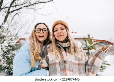 Portrait of two caucasian women friends having fun, standing outdoor near van during the snowfall.