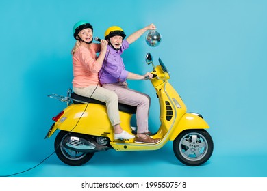 Portrait of two cheerful elderly retired pensioners riding moped singing hit having fun isolated over bright blue color background