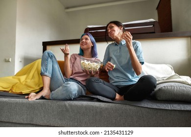 Portrait Of Two Cheerful Women Sitting On Couch At Home, Watching Comedy TV Show, Lauching And Eating Popcorn. Lesbian Couple Spending Time Together After Working Day. Stress Relief Activities.