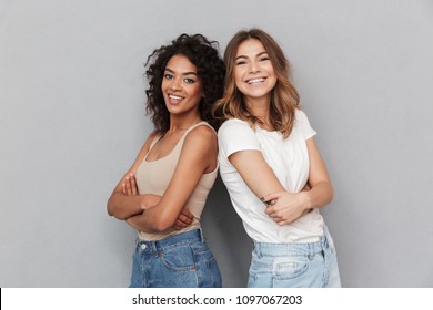 Portrait of two cheerful young women standing together and looking at camera isolated over gray background - Shutterstock ID 1097067203