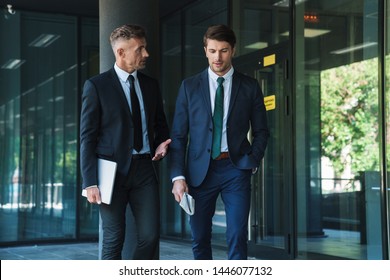 Portrait Of Two Concentrated Businessmen Partners Dressed In Formal Suit Walking And Having Conversation Outside Job Center During Working Meeting