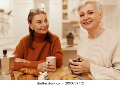 Portrait Of Two Confident Successful Women In Their 50s Sitting At Cozy Cafe Having Breakfast Together, Drinking Morning Coffee With Baking Goods, Talking, Sharing News. People And Lifestyle