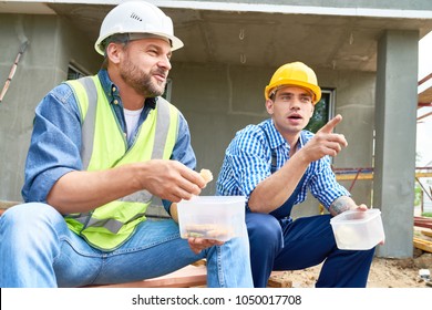 Portrait Of Two Construction Workers Taking Break On Site Eating Lunch Out Of Plastic Containers Outdoors