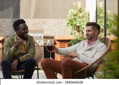 Portrait Of Two Contemporary Men Enjoying Wine While Relaxing In Lounge Chairs At Outdoor Terrace, Copy Space