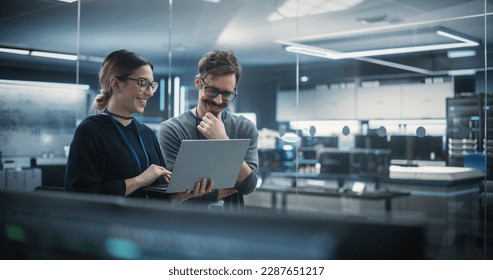 Portrait of Two Creative Young Female and Male Engineers Using Laptop Computer to Analyze and Discuss How to Proceed with the Artificial Intelligence Software. Standing in High Tech Research Office - Powered by Shutterstock