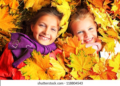 Portrait of two cute girls sisters lying on the leaves at the autumn park.
