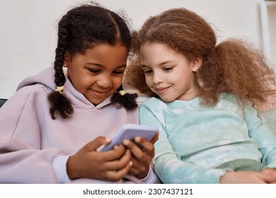 Portrait of two cute little girls using smartphone together and playing mobile games - Powered by Shutterstock