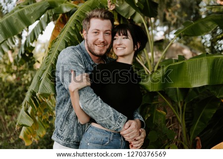 Portrait of Two Cute Modern Caucasian Beautiful Young Adult Guy Boyfriend Lady Girlfriend Couple Hugging and Kissing in Love in Nature with Green Plants Trees in the Outdoor Park