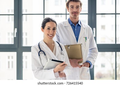 Portrait Of Two Determined Physicians Wearing White Medical Gowns While Looking At Camera With Serious Facial Expression In A Modern Health Center