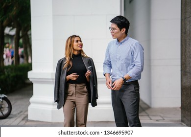 Portrait Of Two Diverse Asian Business People (colleagues Meeting For Lunch) Walking In The City (Singapore River). One Is A Korean Man, The Other A Malay Woman. They Are Both Smiling As They Chat.