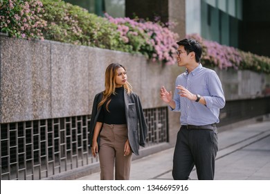 Portrait Of Two Diverse Asian Business People (colleagues Meeting For Lunch) Walking In The City (Singapore River). One Is A Korean Man, The Other A Malay Woman. They Are Both Smiling As They Chat.