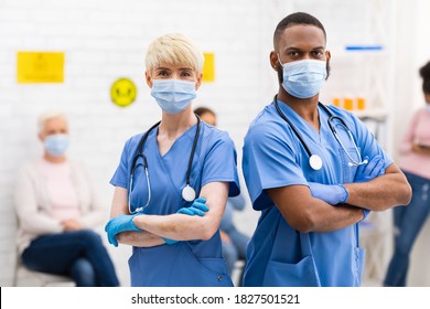 Portrait Of Two Diverse Doctors In Protective Masks Posing Looking At Camera Standing In Hospital Waiting Room With Patients. Medical Clinic Staff, Physician Doctor And Nurse Profession Concept