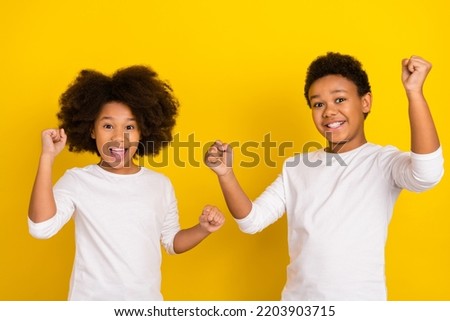 Portrait of two excited successful pupils raise fists celebrate triumph isolated on yellow color background