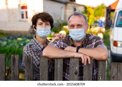 Portrait Of Two Farmers Wearing Protective Masks At The Fence Of Their Country House