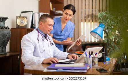 Portrait of two fellow doctors discussing clinical diagnosis of patients and filling up medical forms on laptop in office - Shutterstock ID 2002273169