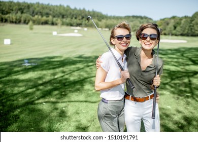 Portrait Of A Two Female Best Friends Standing With Golf Equipment On A Playing Course, Talking And Having Fun During A Game On A Sunny Day