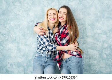 Portrait of two female friends in checkered shirts and jeans having fun together on the blue painted wall background