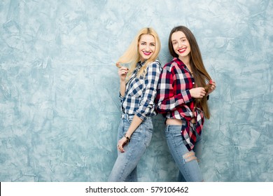Portrait of two female friends in checkered shirts and jeans together on the blue painted wall background