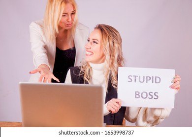 Portrait Of Two Female Worker Laughing And Talking About Boss With Sign Stupid Boss. 