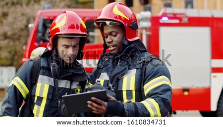 Portrait of two firefighters in fire fighting operation, fireman in protective clothing and helmet using tablet computer in action fighting. 