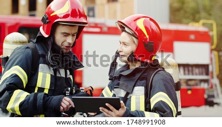 Portrait of two firefighters in fire fighting operation, fireman in protective clothing and helmet using tablet computer in action fighting. 